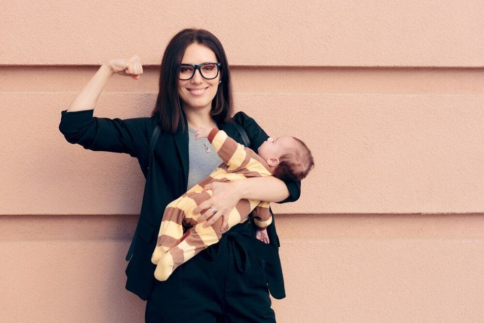 Strong independent business woman holding a baby and showing her biceps 
