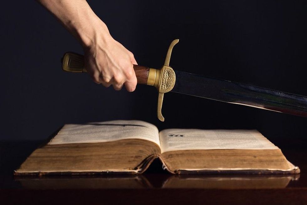 Strong male hand with sword on top of open Book