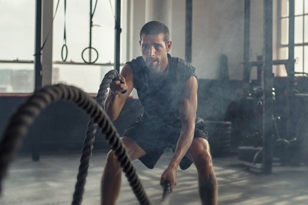 Strong young man working out with battle ropes in a crossfit gym.