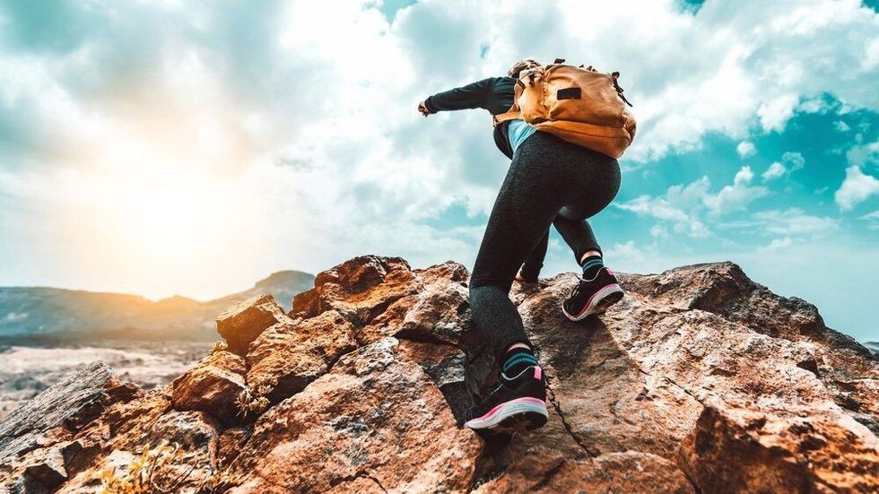 Successful hiker with backpack climbing the mountain on sunset.