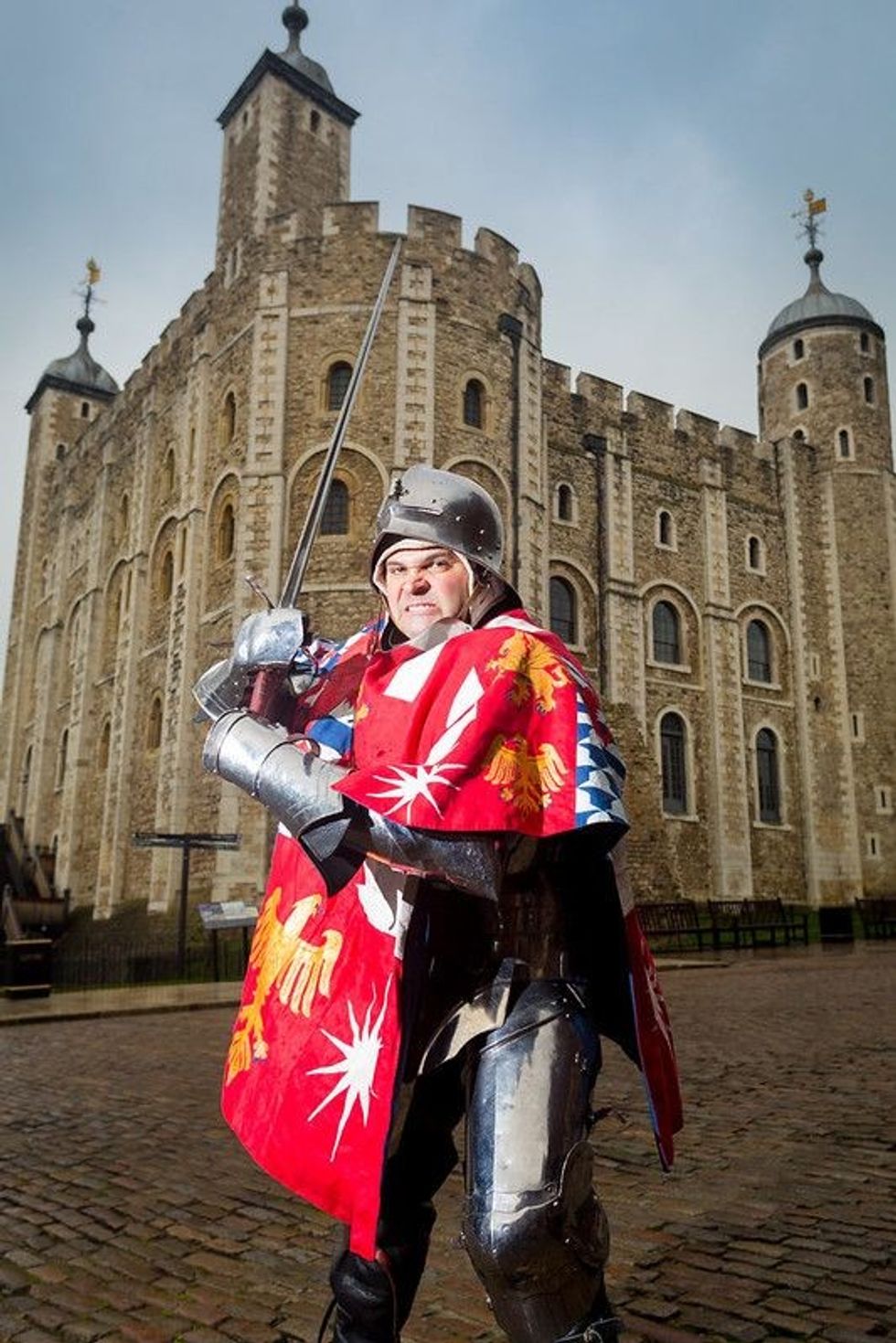Sword-wielding knight strikes a pose with a medieval-era building in the background