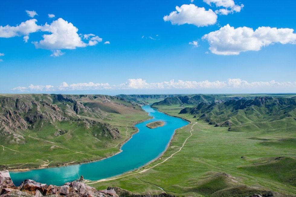 The beautiful colourful spring panorama of Ili river, rocks and the road in the steppe.