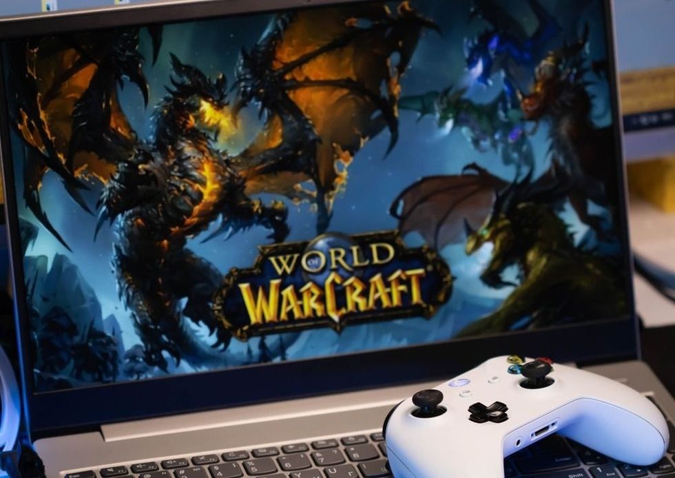 The computer game World of Warcraft is on the laptop screen, next to it lies a white Xbox game joystick.