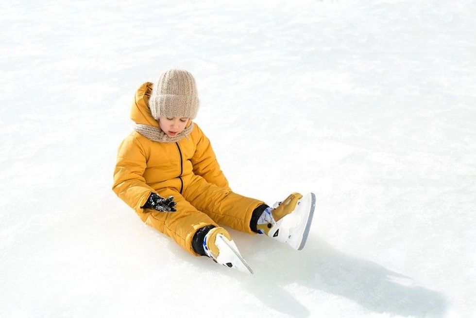 The girl fell on the ice, taking her first steps on skates. A child learns to skate. A child sits on an ice rink and examines mittens that were injured during the fall. Ice skating season on the pond