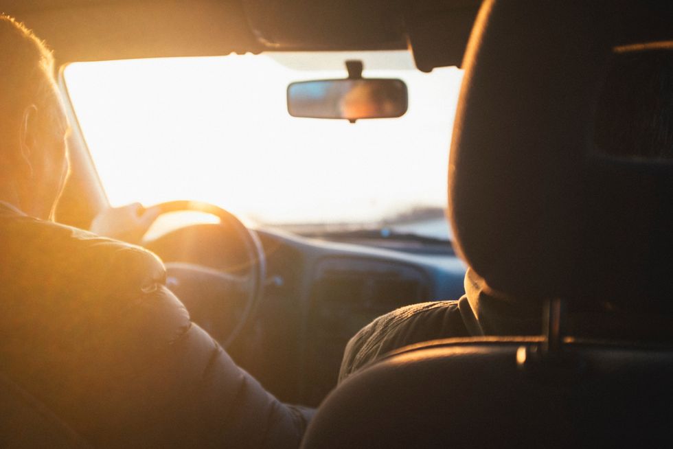The interior of a car during sunset, with warm sunlight flooding the cabin and a person at the steering wheel, driving towards the bright horizon.