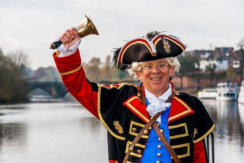 The Town Crier of the City of Chester, holding his bell and shouting the news on the town's streets.