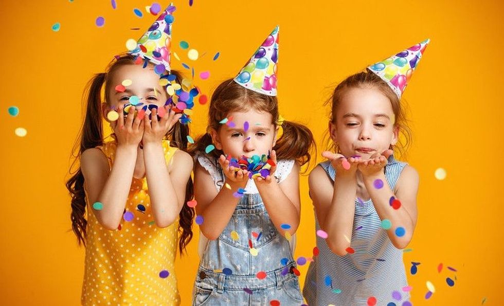 Three adorable little girls wearing party hats and playing happily with confetti