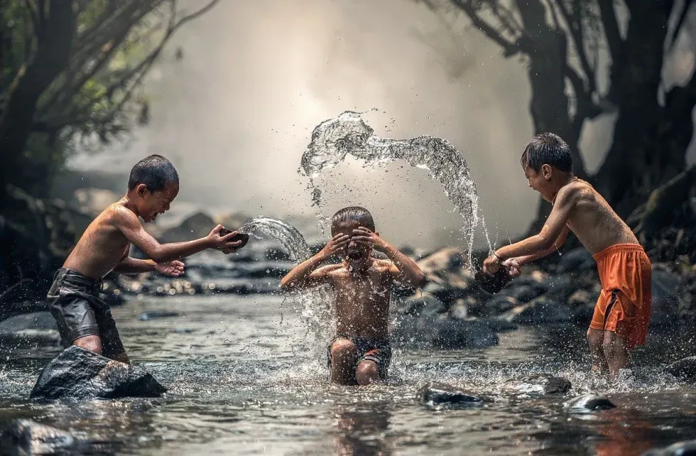 Three children playing in a pool of water and splashing water around.