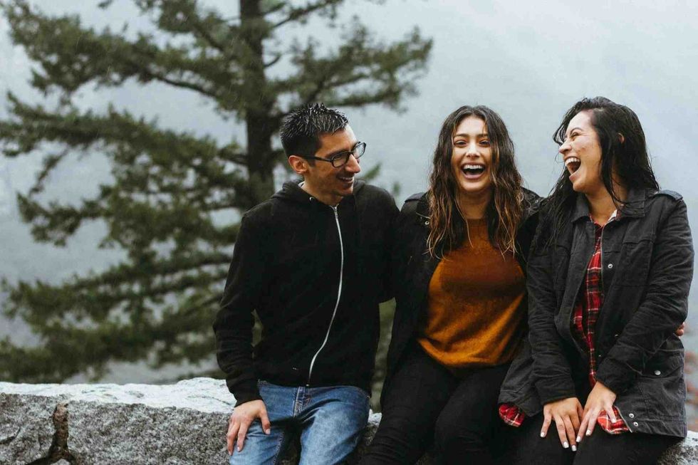 Three friends sitting outdoors, sharing a joyful moment with laughter that might be from updog jokes.