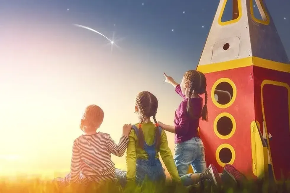 Three kids playing with a large toy rocket, gazing up at the amazing night sky looking at stars.