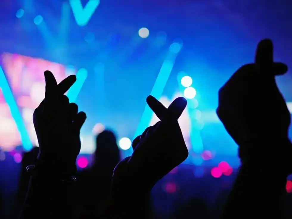 Three people with folded hand denoting heart in a Kpop concert