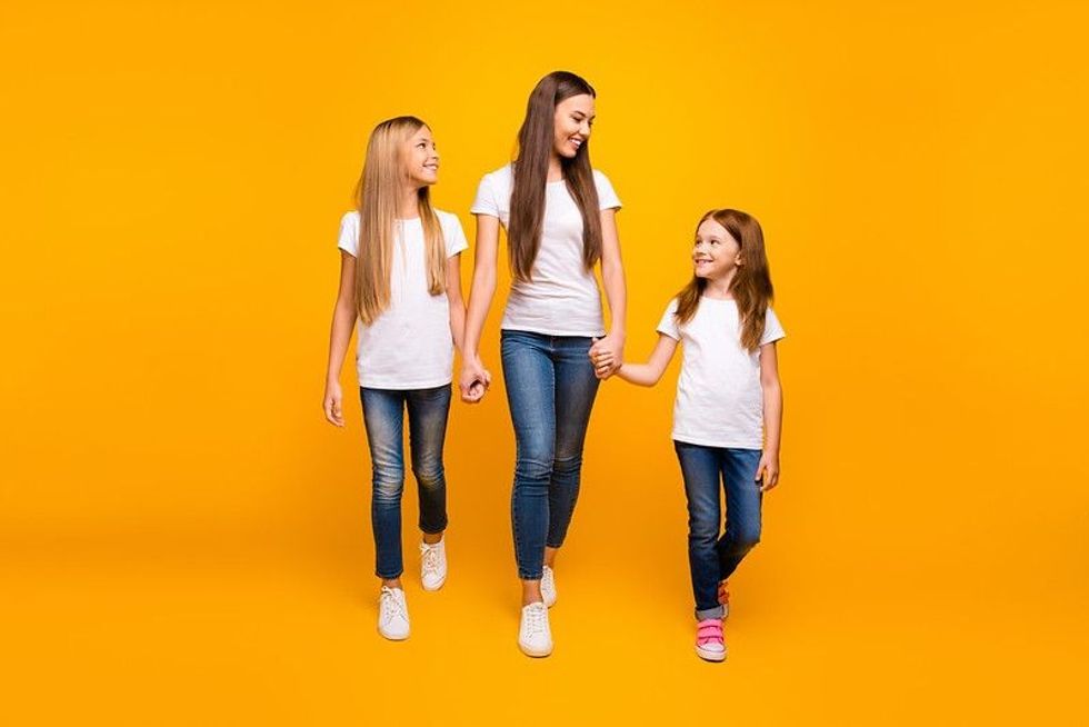 Three sisters holding hands while walking.