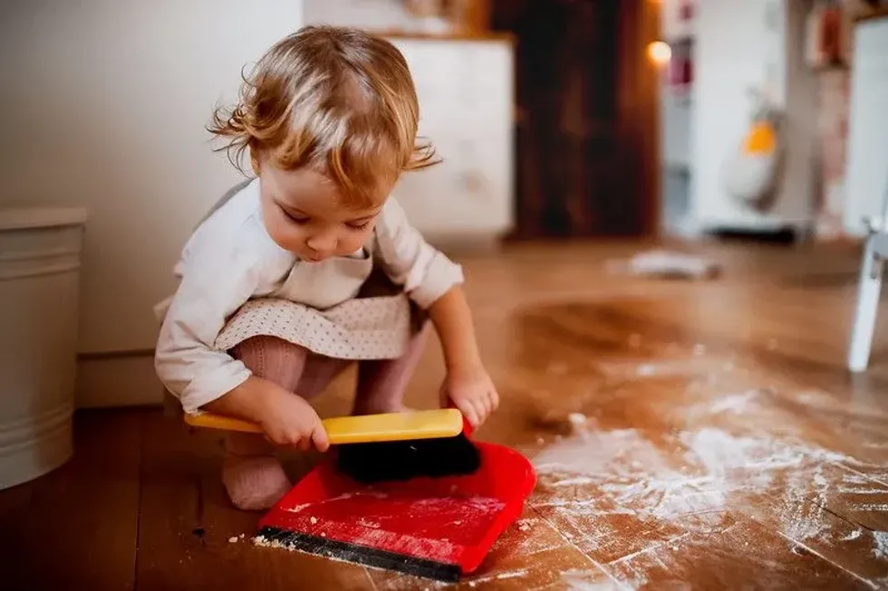 Toddler using a dustpan and brush on the kitchen floor.
