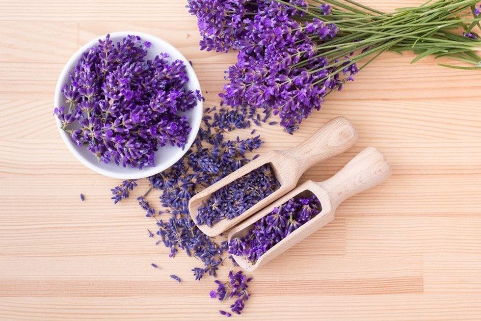 Top view of a bowl and wooden spoons with dried and fresh lavender flowers and a bouquet of lavender on a wooden background.