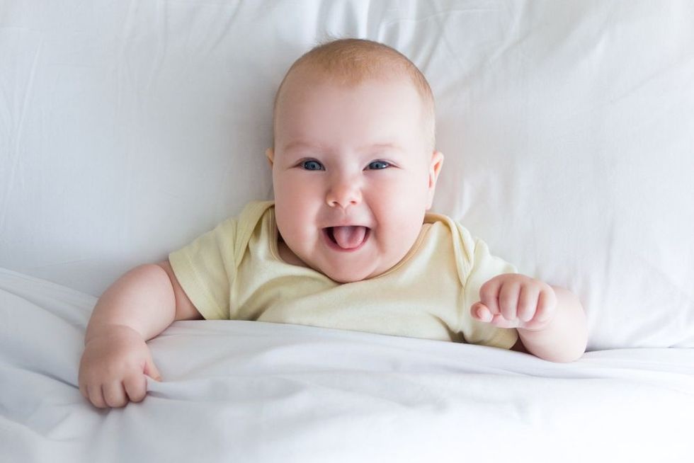 top view of funny little baby girl lying on the bed under blanket