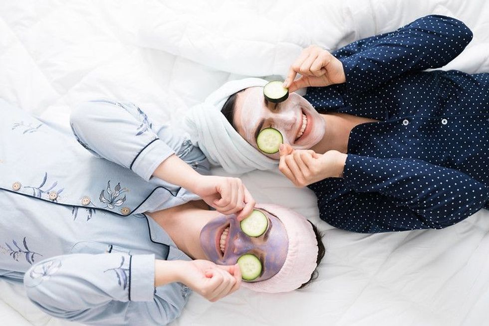 Top view of two excited women friends in bed putting cucumber slices in their eyes