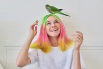 Trendy fashionable with brightly colored hairstyle teenager with green young parrot quaker on his head