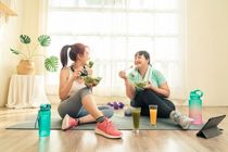 Two Asian women body size different in sport wear sitting healthy eating vegetable salad after exercise at home together.