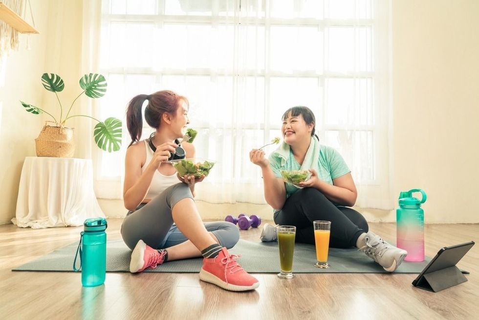 Two Asian women body size different in sport wear sitting healthy eating vegetable salad after exercise at home together.