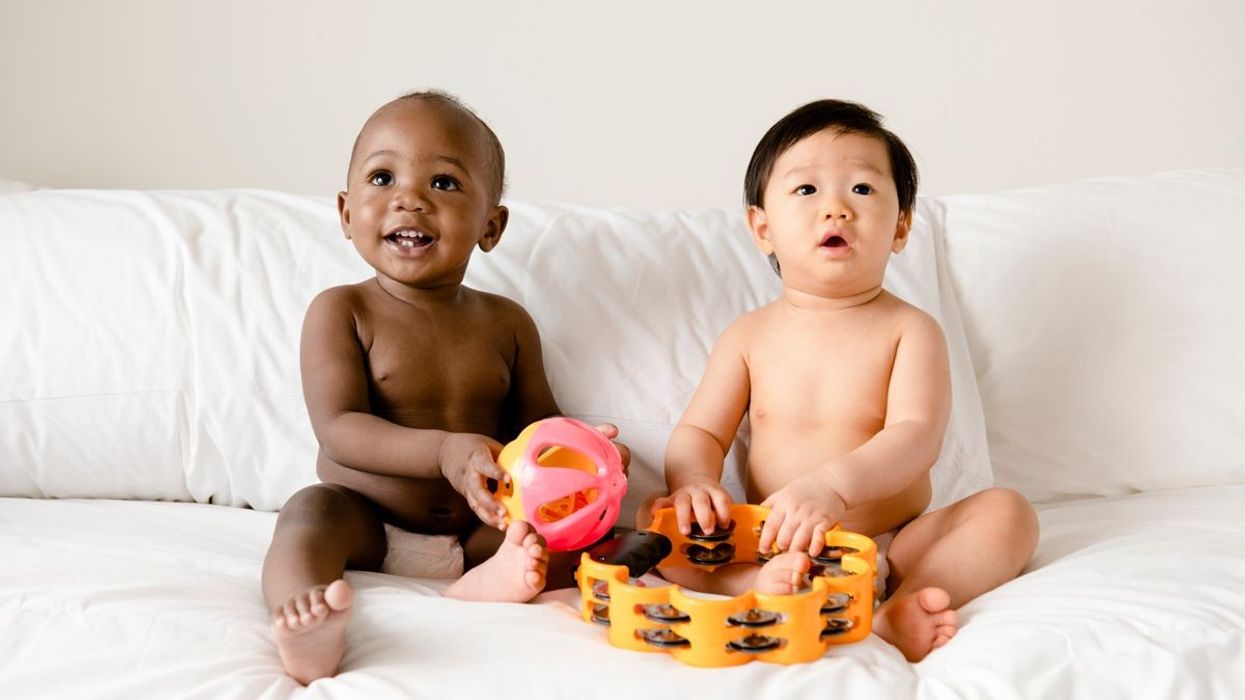 Two babies sitting on a bed, playing with musical toys, encapsulating the harmony of a melodic baby name.