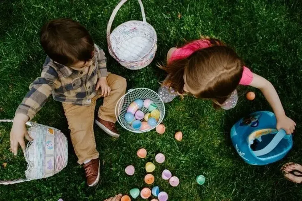 Two children playing on the grass and picking up colorful Easter eggs.