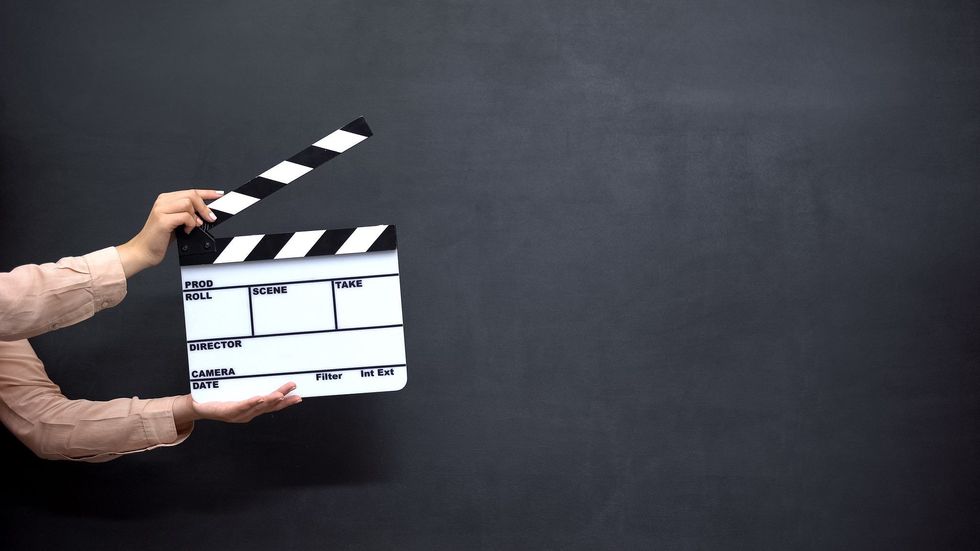 Two hands holding a clapperboard against a black background.