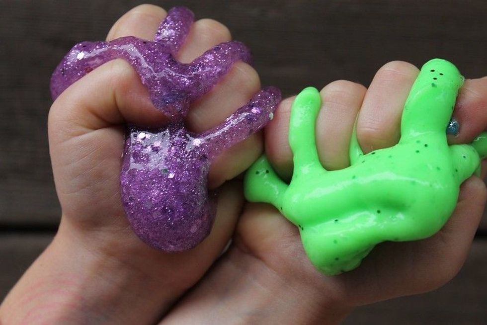 Two hands squeezing purple and green slime.