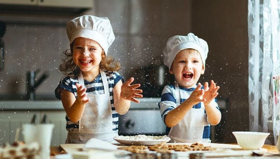 Two kids in aprons and caps in a kitchen setting, laughing happily and depicting the joy derived from baking puns.