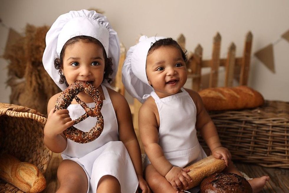 Two kids in chef costume eating pretzel.