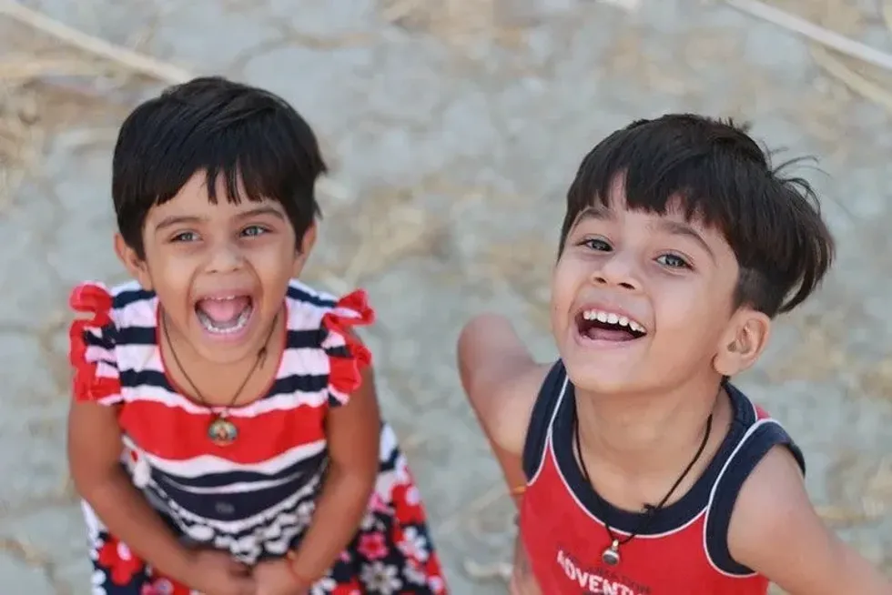 Two kids standing, looking up, smiling, and laughing.