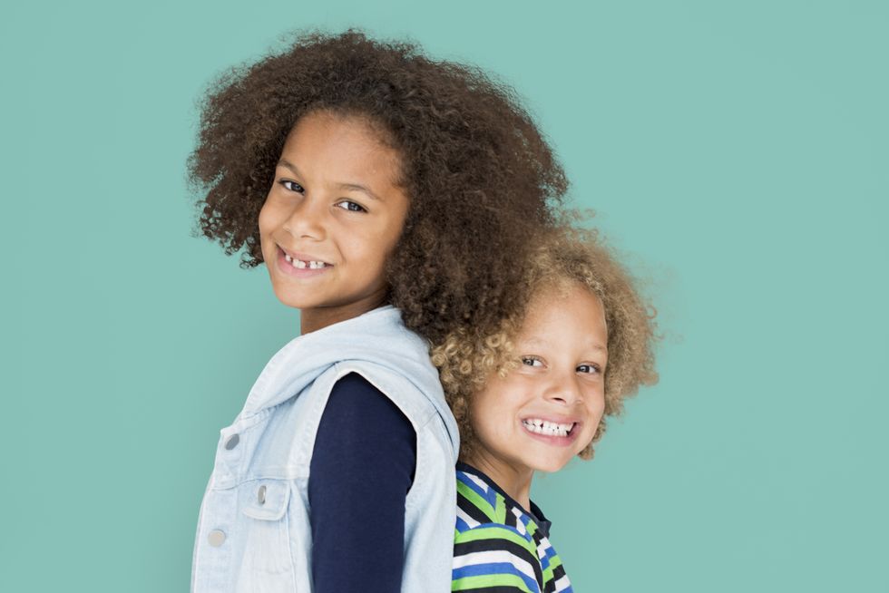 Two kids with black and blonde curly hair smiling and posing for the camera.