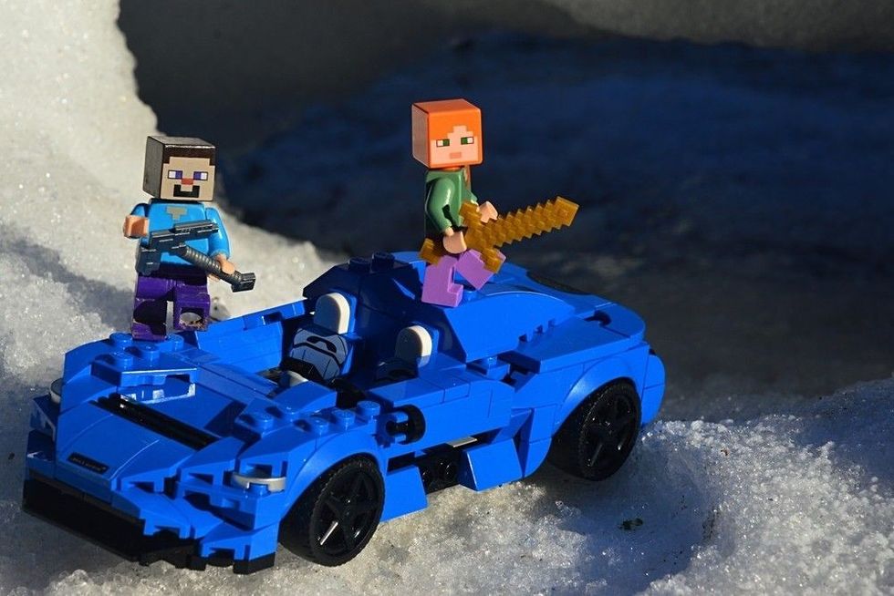 Two Minecraft character, one standing on a car and holding a sword and the other holding a pickaxe.