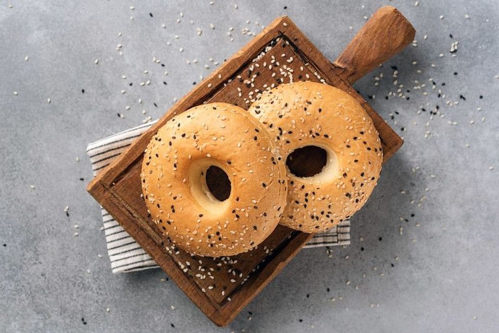 Two sesame bagels on wooden cutting board.