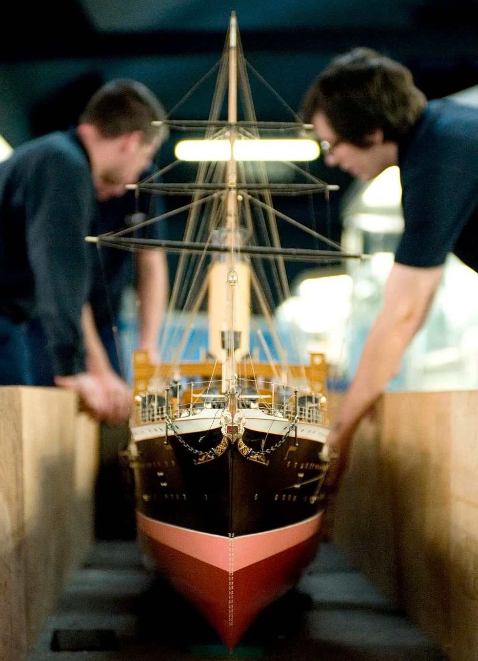 Two staff members at Riverside Museum holding a large model of a ship.