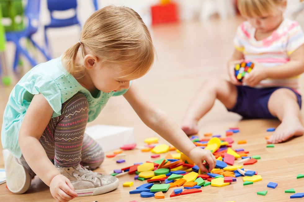 Two sweet toddler girls playing with puzzle pieces on the floor of their preschool classroom. The puzzle pieces are colorful and the preschoolers are focused on the task at hand.