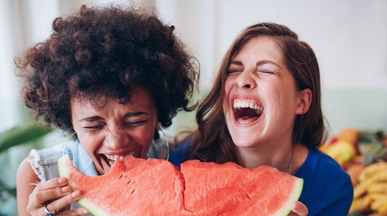 Two young girls eating a watermelon slice and laughing together.