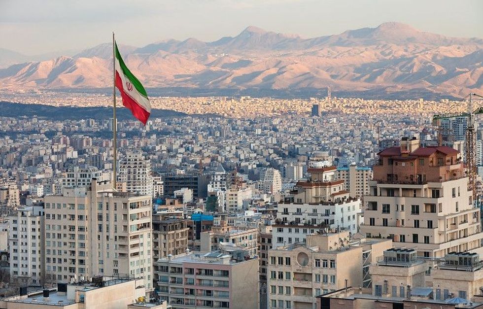 Waving Iran flag above skyline of Tehran at sunset