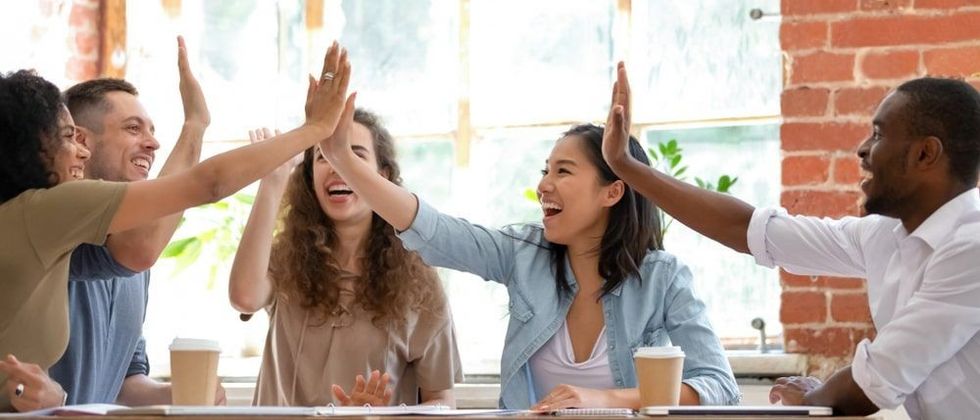 Wide horizontal image multicultural cheerful businesspeople sitting together at meeting giving high five gesture feels excited happy