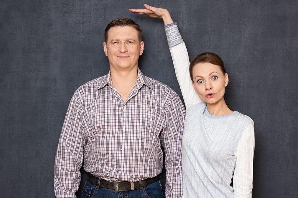 Woman extending hand over a man's head to show his tall height.