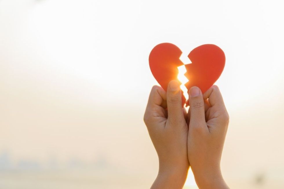Woman hand holding broken paper red heart on sunset.