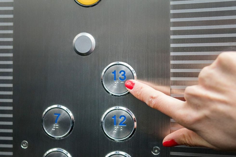 Woman in elevator or lift is pressing the button to go on 13th floor