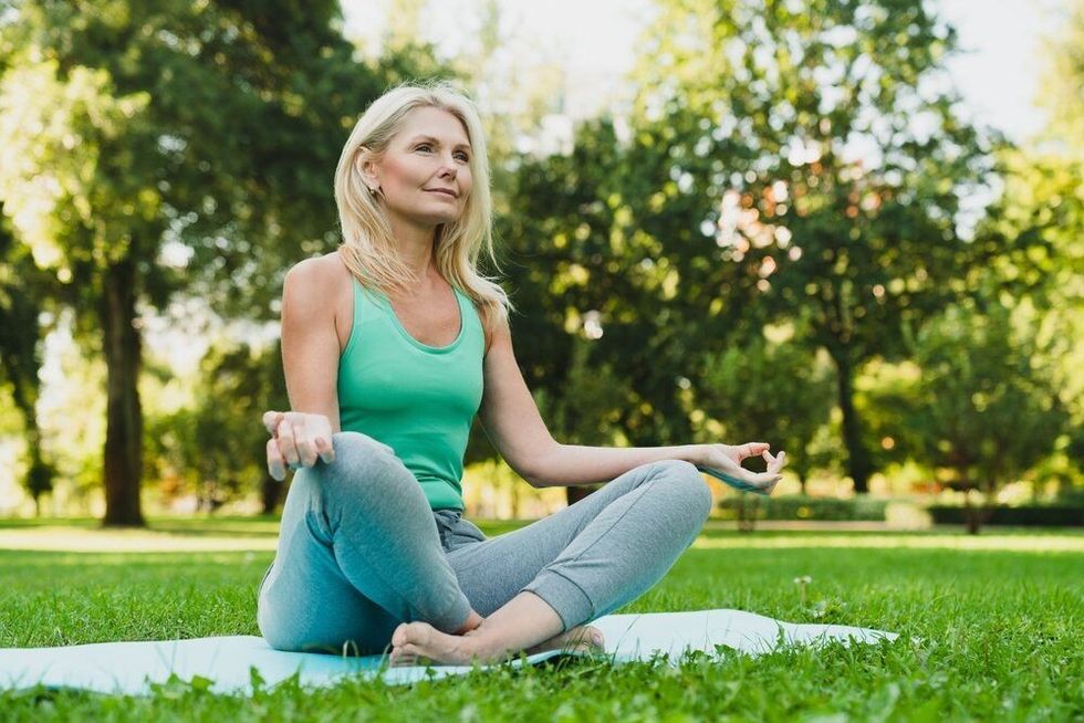 Woman meditating in a garden on a yoga mat looking relaxed