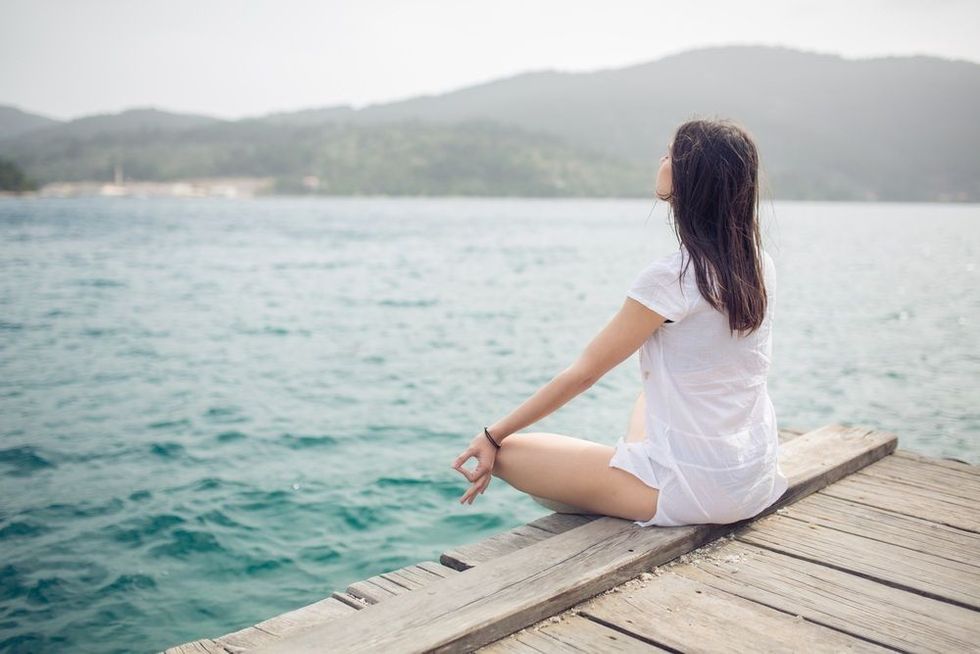 Woman meditating in sitting yoga position on pier.