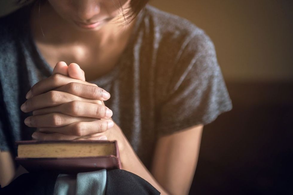 Woman praying with her hands together over a closed Bible.