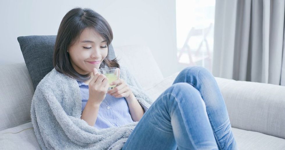Woman sitting on a couch with a cup wrapped in a blanket
