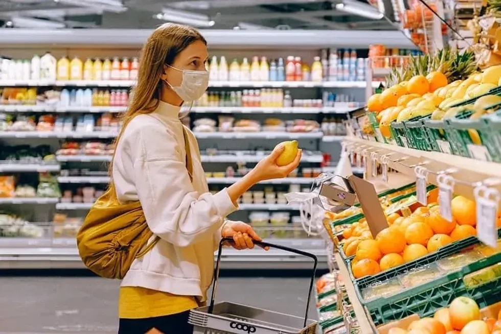 Woman wearing a white face mask in the supermarket buying a lemon.