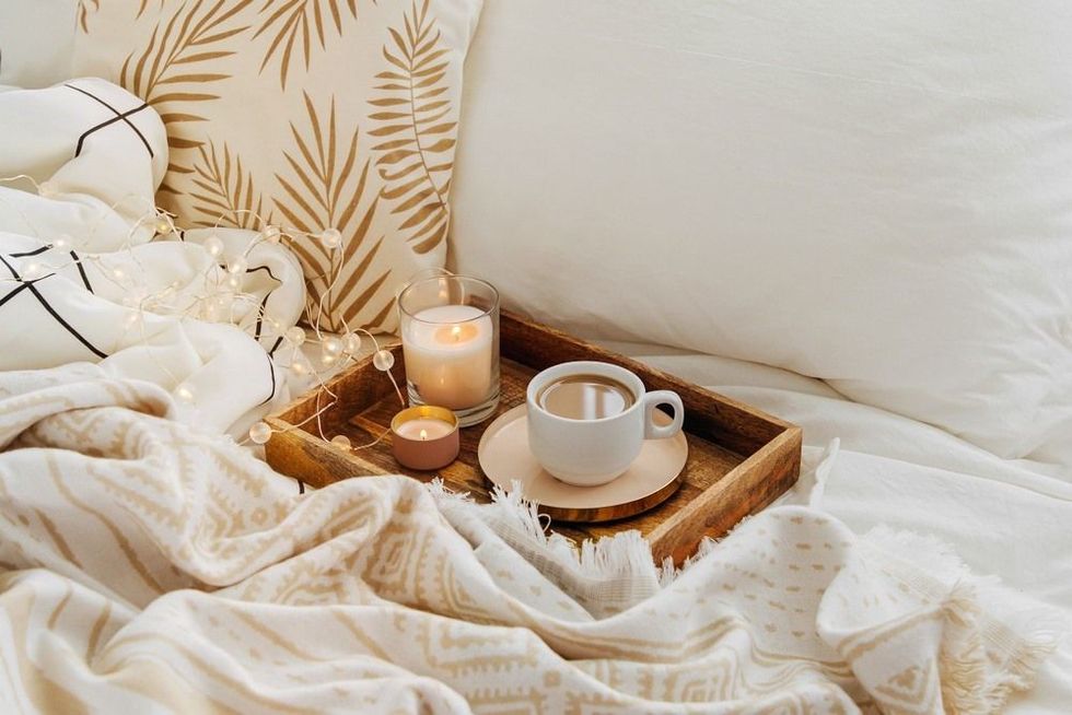 Wooden tray of coffee and candles on bed. White bedding sheets with striped blanket and pillow.