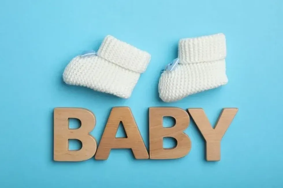 Wooden word BABY with two knitted white shoes on top on a blue blackground