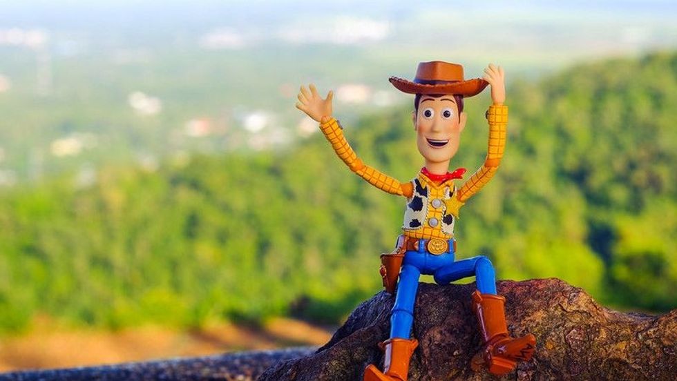 Woody from Toy Story animated movie sitting on the rock waving at camera.