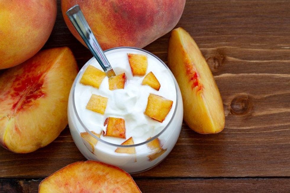 Yogurt with slices of fresh peaches and whole peaches on a wooden background